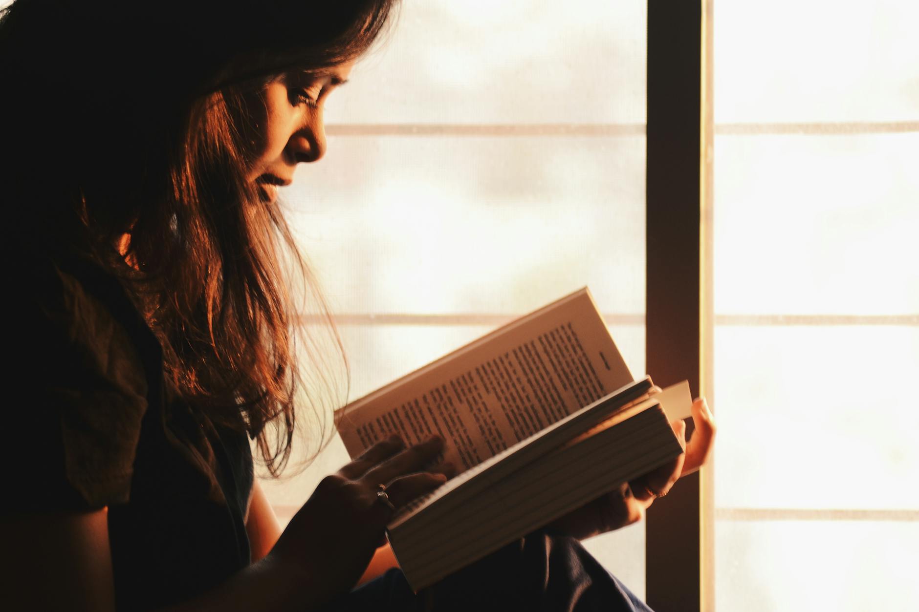 woman reading a book by the window in soft light, quiet and cozy atmosphere